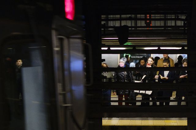A woman in a crowd on a subway platform wears a subway over her face